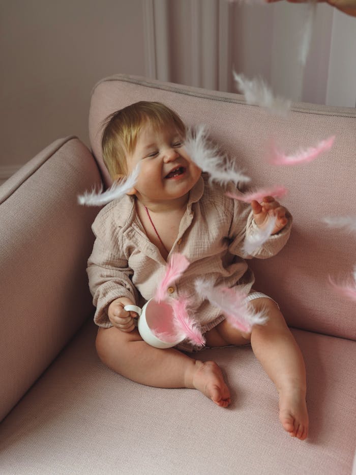 pexels photo 15919225 Cute baby girl joyfully playing with soft feathers on a cozy sofa indoors.