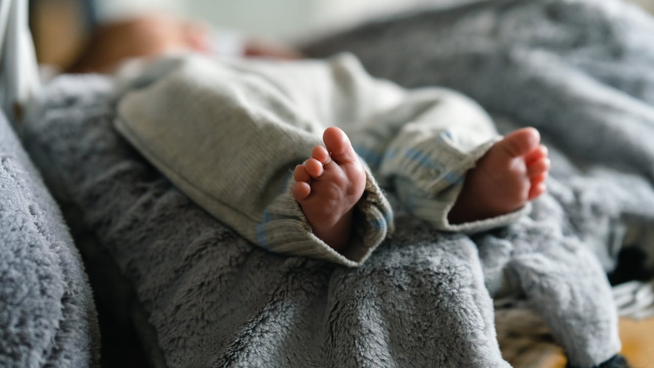 Adorable close-up of baby feet in cozy clothing, resting on a soft blanket.